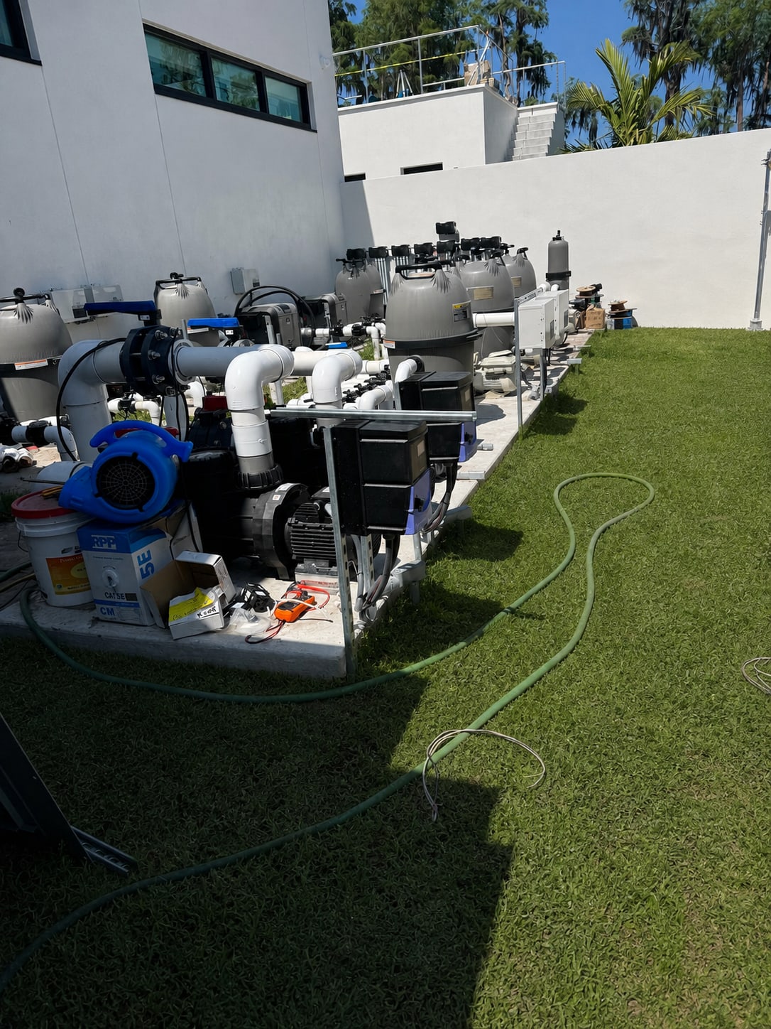 Multi-pump pool equipment system with filters, plumbing, valves, and controls beside a maintained lawn